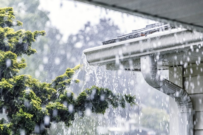 Why You Need Whole-House Humidity Control. Photo of the outdoors downpouring rain, overflowing the gutters of a house.